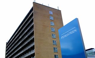Et hospital med et skilt foran, hvor der står Aalborg Universitetshospital PSYKIATRIEN