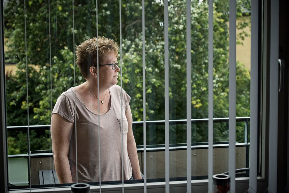Tidligere Sosu-hjælper Jeannette Stripp stående på sin terrasse, fotograferet gennem vinduet
