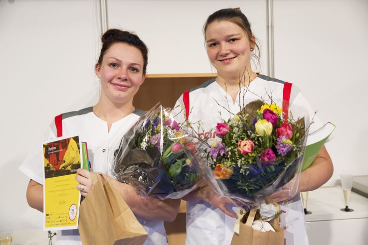 To piger i hvid uniform med blomster og diplom i hånden