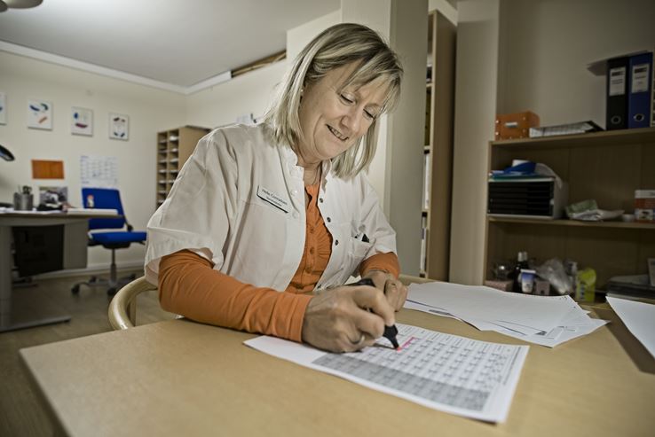 Helle Conradsen sidder ved et skrivebord og markerer nogle ting på et papir med en overstregningstus