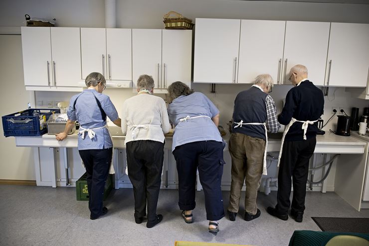 Tre kvinder og to mænd står med ryggen til, i et industrikøkken