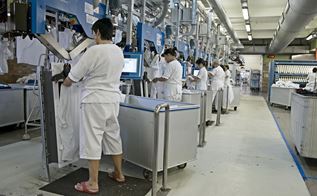 En lang række af ansatte i hvidt arbejdstøj står ved hver deres maskine på vaskeri