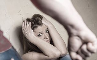Ung kvinde sidder med hænderne om hovedet for at beskytte sig mod voldelig mand