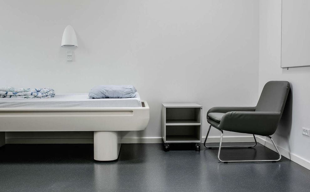En tom seng står på et værelse med en stol og et sengeborg