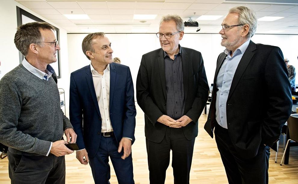 4 mænd snakker sammen i stort mødelokale