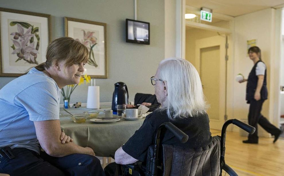 Social- og sundhedsassistent på plejehjem i samtale med dame i kørestol foto: Jørgen True