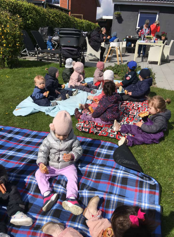 Børn sidder på tæpper uden for.