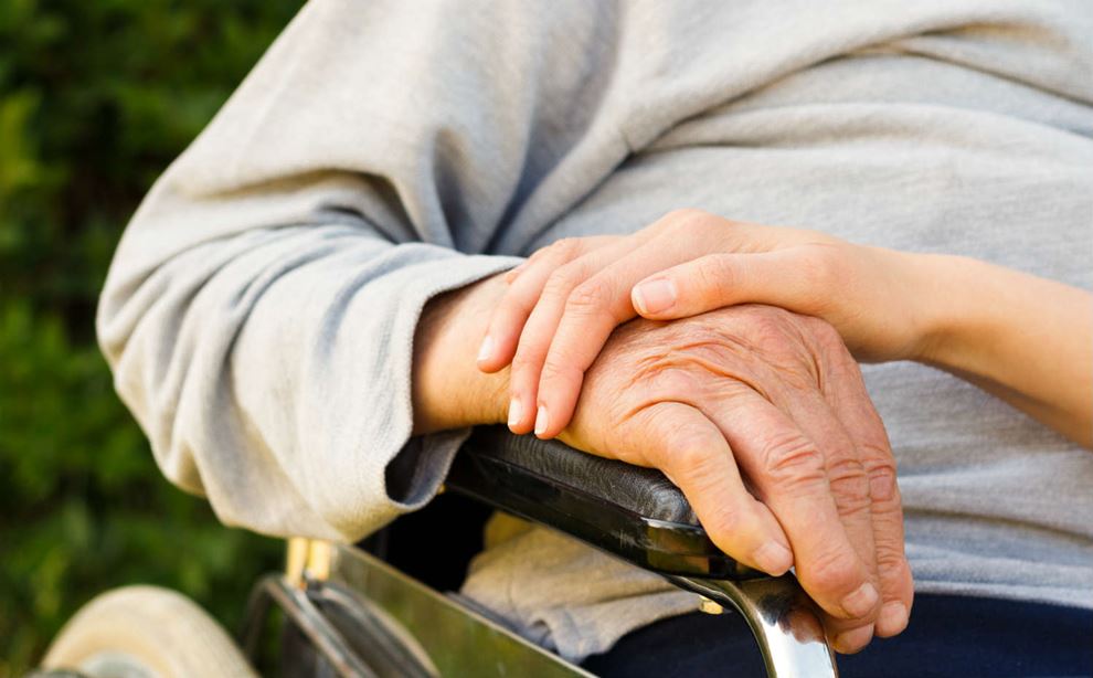 En yngre hånd holder på en ældre hånd på armlænet af en kørestol