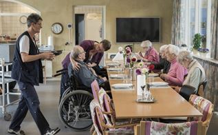 En gruppe ældre mennesker får serveret mad ved et langborg