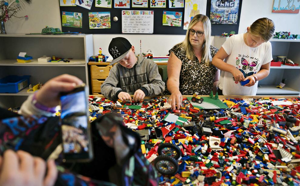 Voksen leger med LEGO med to børn. Mobilskærm i forgrunden.