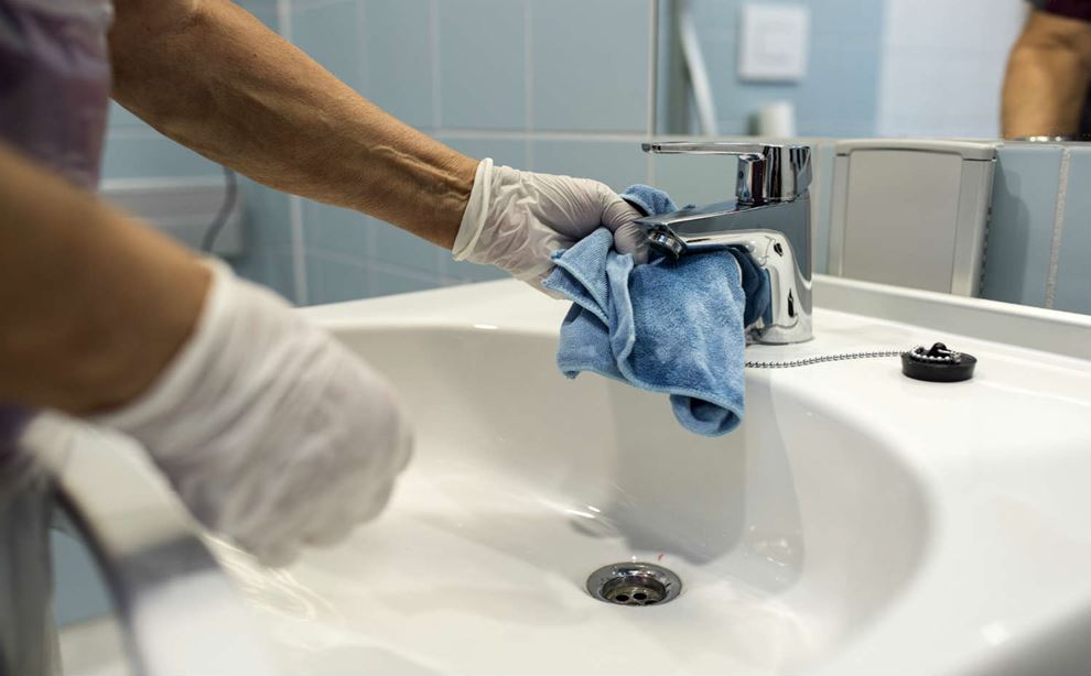 Rengøring af en hvid håndvask med en blå klud