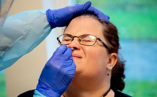 Kvinde bliver testet for corona i næsen af person med blå handsker på