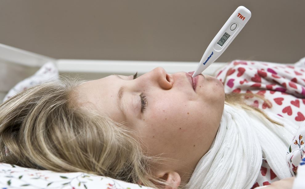 Kvinde ligger i sengen med termometer i munden