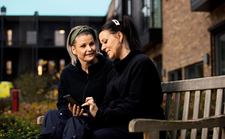 To kvinder sidder på en bænk og taler sammen